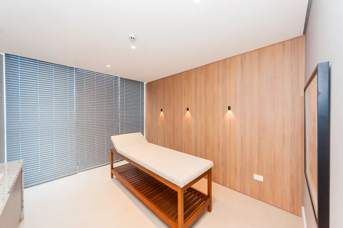 Sala de massagem com maca, painel de madeira e persianas