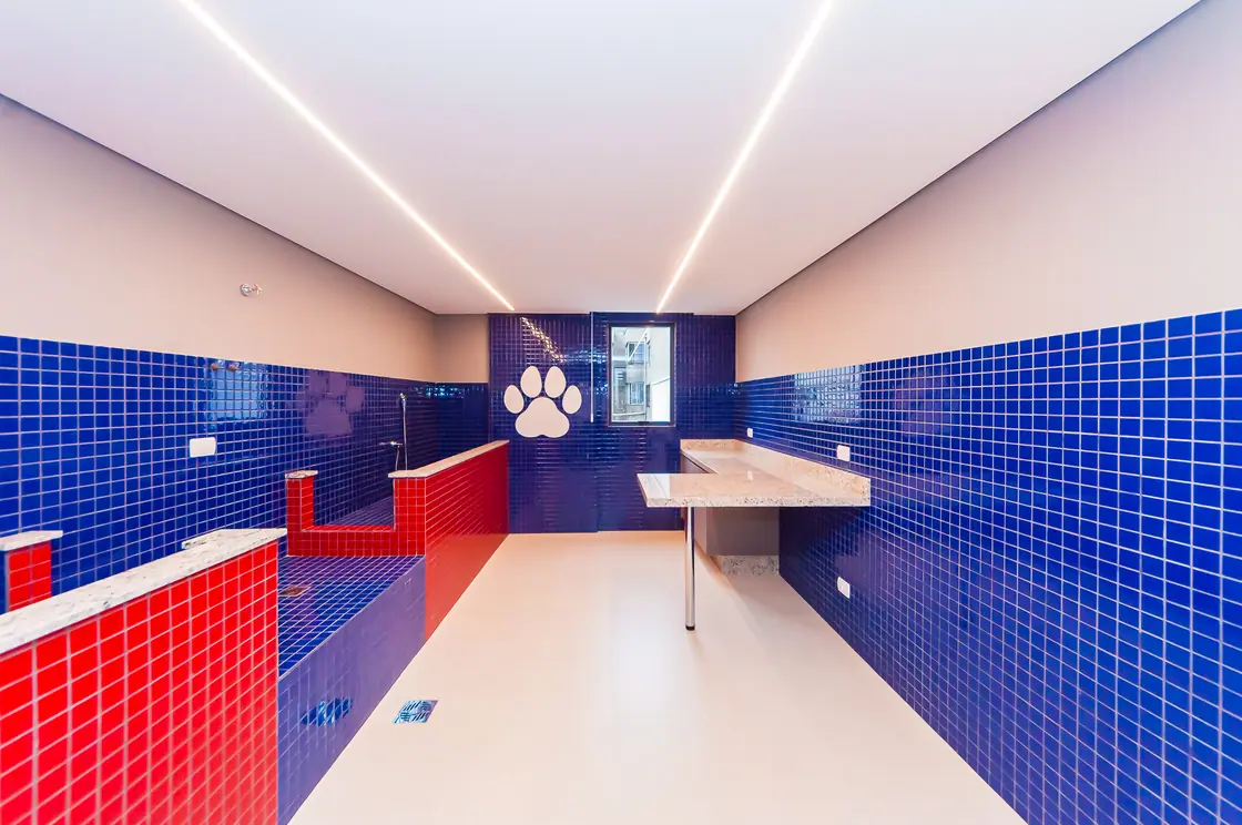 Espaço pet care em pastilhas azuis e vermelhas, com banheira e bancada