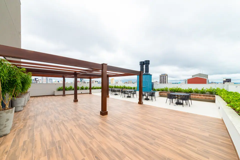 Deck ao ar livre com piso de madeira, mesas e vista para os prédios do Centro
