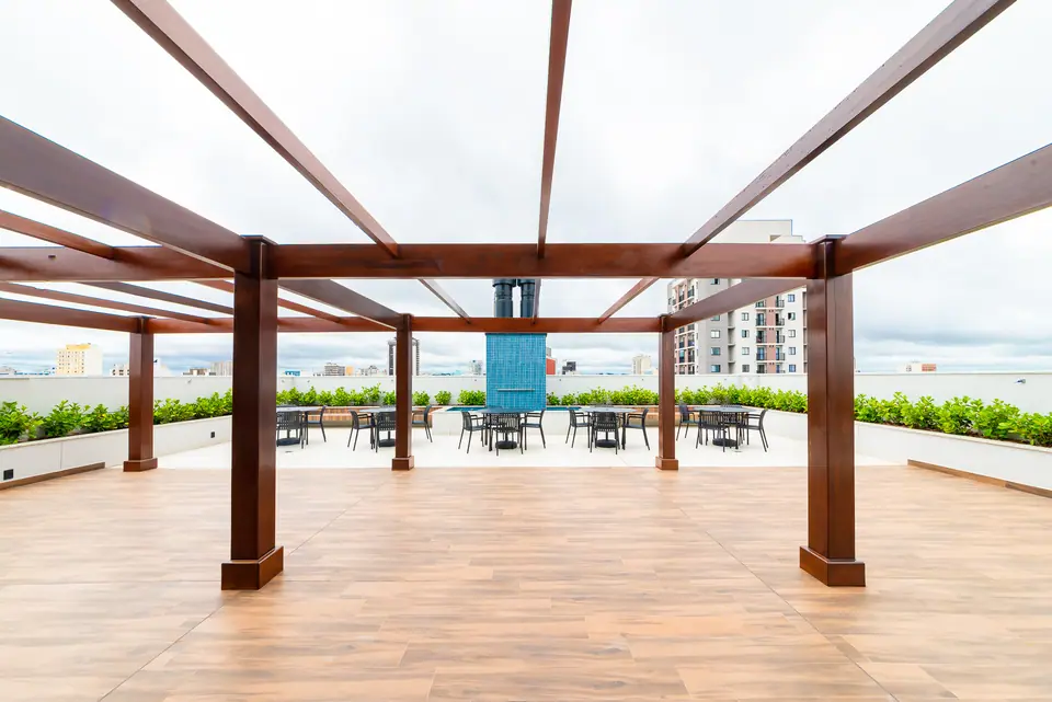 Praça de convivência sob pergolado de madeira com deck e jardineiras