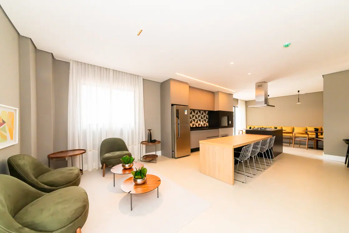 Salão de festas com lounge de poltronas, mesa comunitária e cozinha integrada