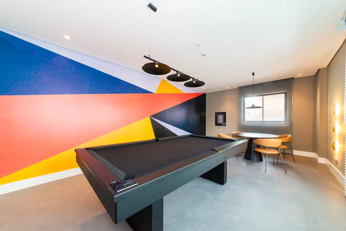 Salão de jogos com mesa de sinuca e mural geométrico